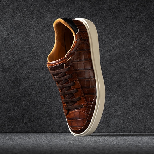 A pair of brown suede cap-toe oxford boots displayed vertically, with one sole facing forward.