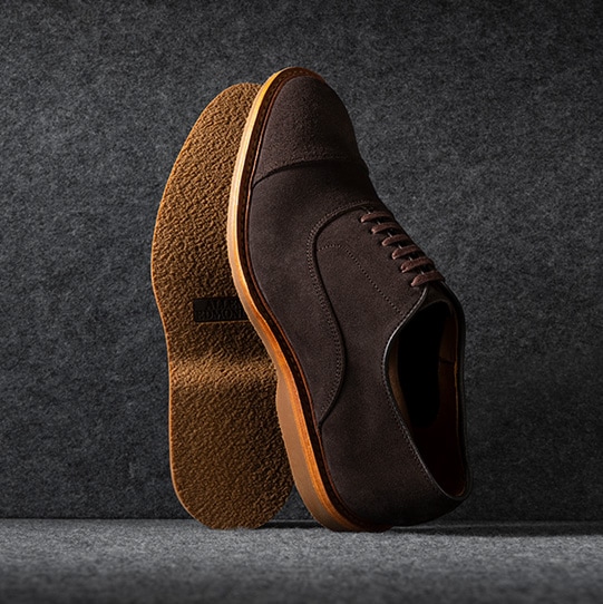 A pair of brown leather derby dress shoes, with one shoe laying on its side to highlight the lug sole. The Allen Edmonds Reserve logo is shown in the top right corner.