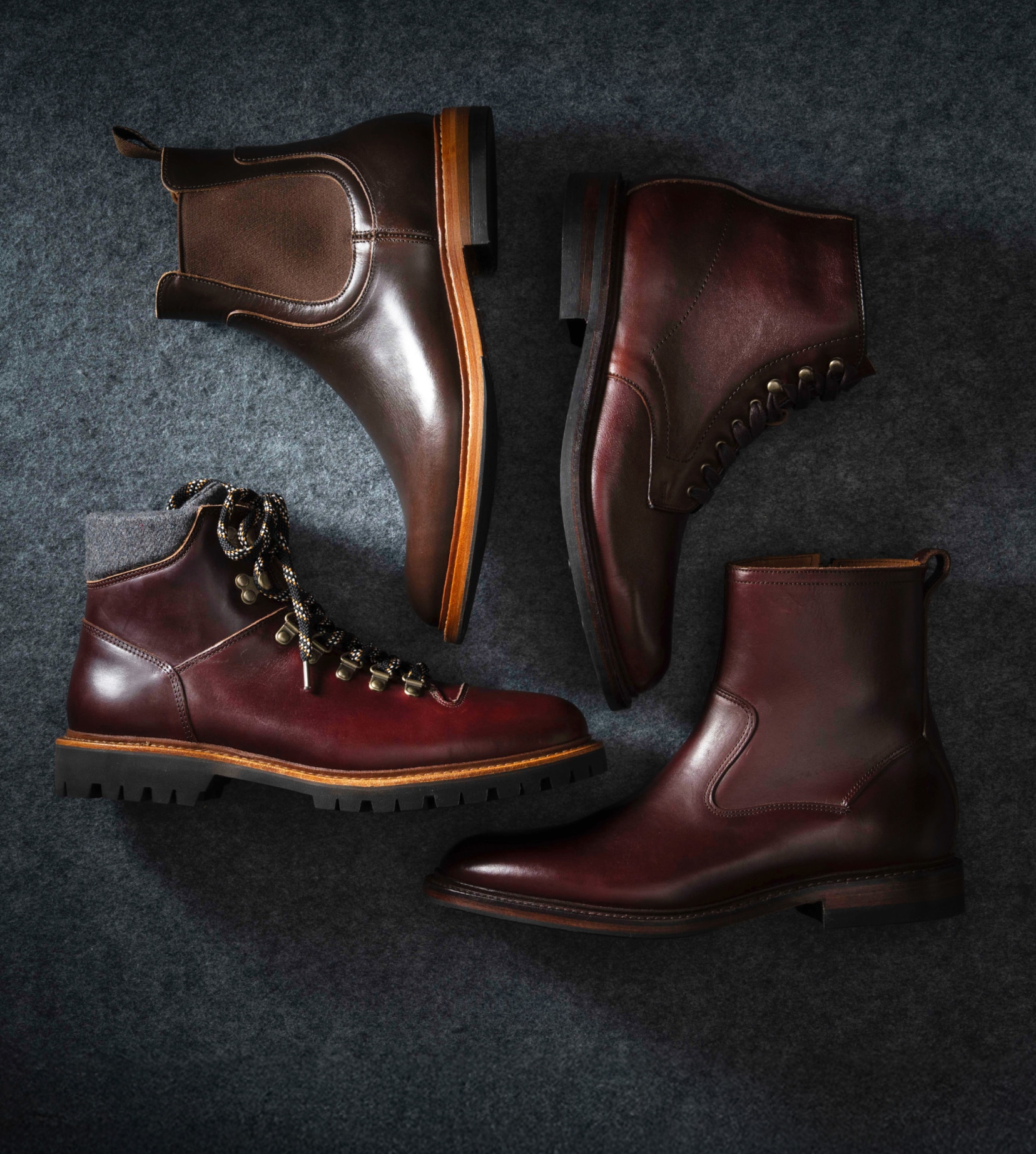 Four different styles of men’s boots, including a hiking boot, lace-up boot, zip-up boot, and a Chelsea boot. Each boot is made from burgundy leather.Quatre styles différents de bottes pour hommes, dont une botte de randonnée, une botte à lacets, une botte zippée et une botte Chelsea. Chaque botte est fabriquée en cuir bordeaux.