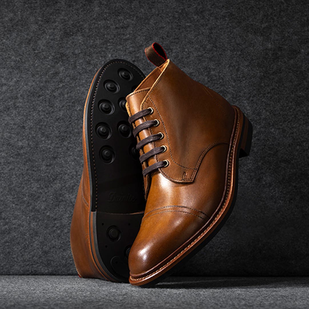 A pair of brown suede cap-toe oxford boots displayed vertically, with one sole facing forward.