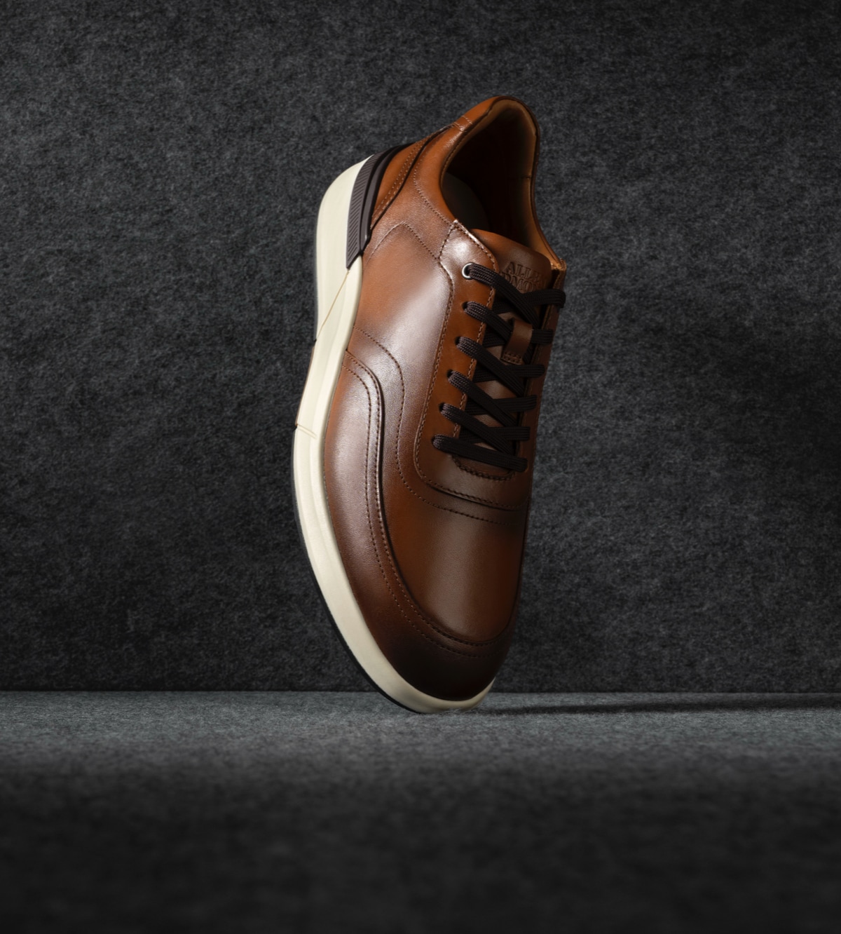 A men’s brown leather sneaker displayed vertically with the toe facing downward. / Une basket en cuir marron pour hommes présentée verticalement avec la pointe tournée vers le bas.