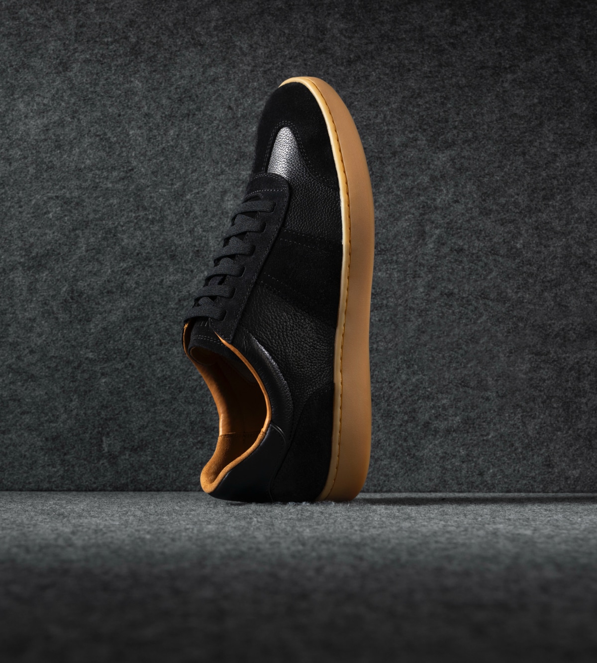 A men’s black sneaker with a gum sole displayed vertically with the toe facing upward. / Une basket noire pour hommes avec une semelle gomme présentée verticalement avec la pointe tournée vers le haut.