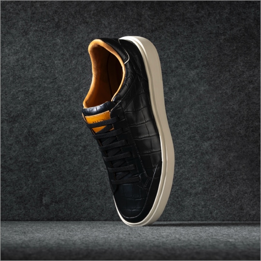A men’s black leather sneaker displayed vertically with the toe facing downward. / Une basket en cuir noir pour hommes présentée verticalement avec la pointe tournée vers le bas.