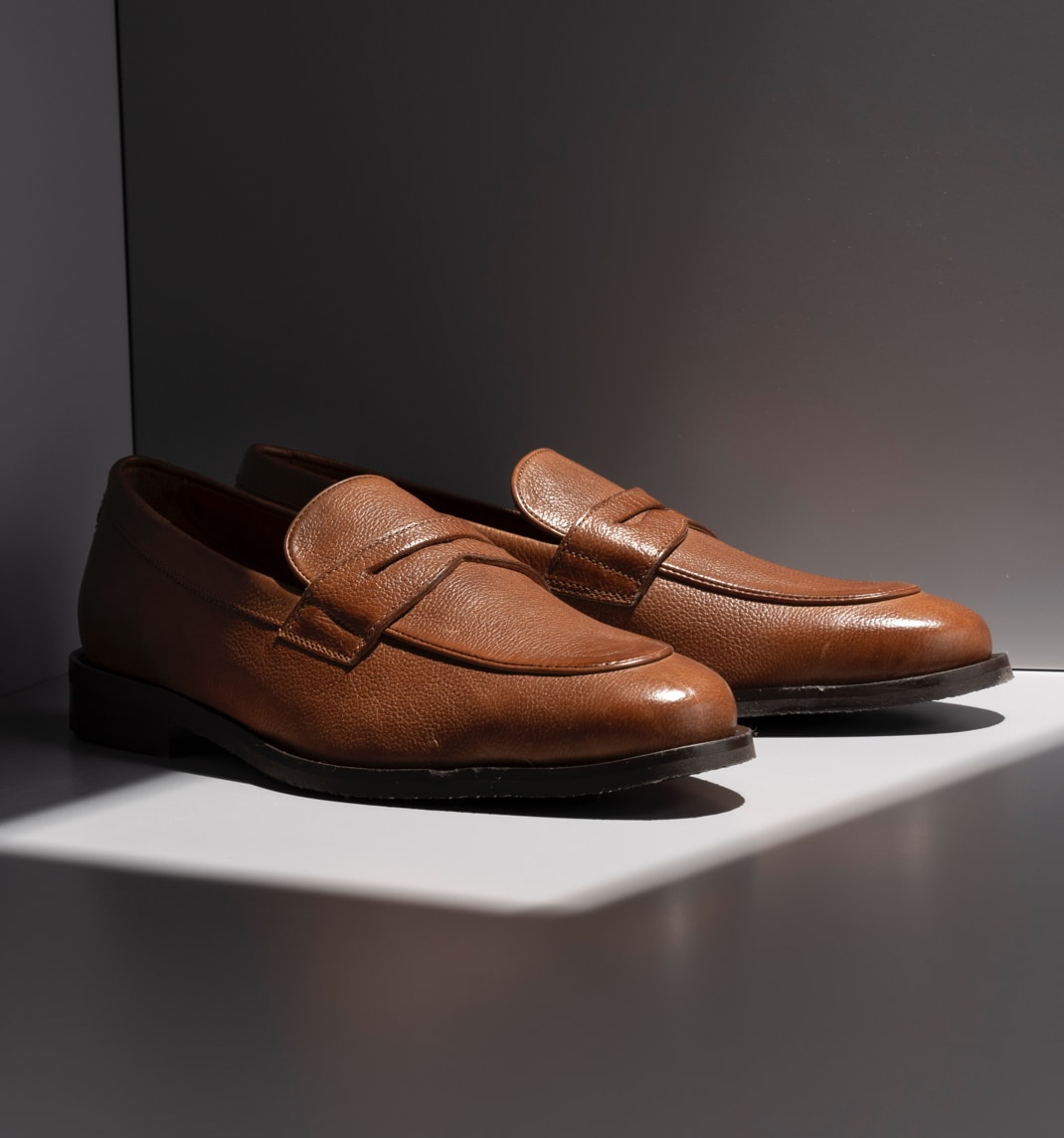An angled view of a pair of men’s brown leather penny loafers.  Vue en coin d'une paire de mocassins en cuir brun pour hommes.