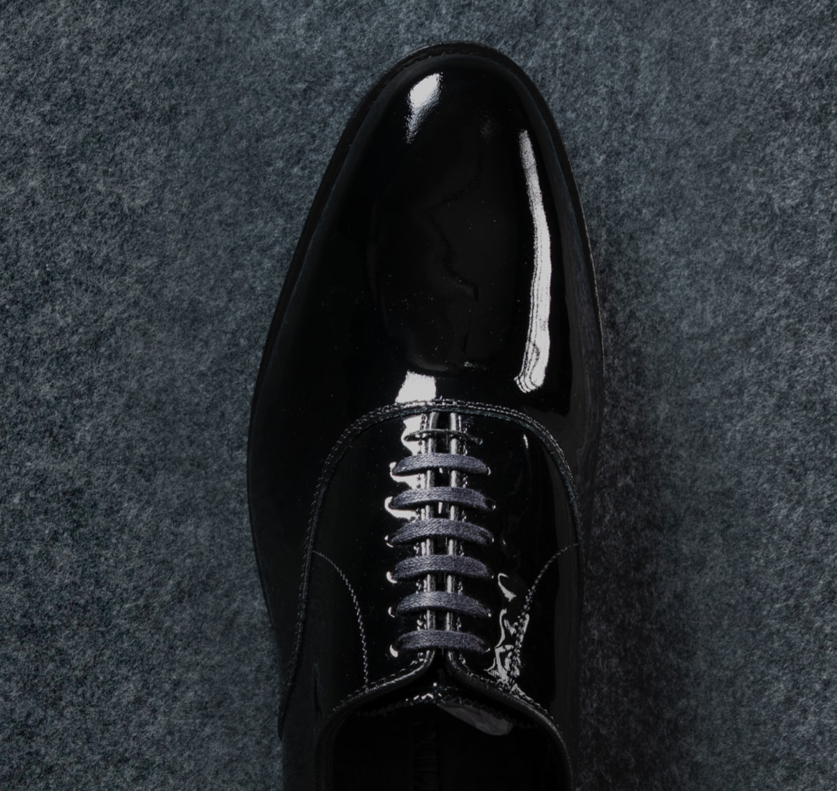 A top view of a black patent leather Oxford dress shoe.  Vue de dessus d'une chaussure habillée Oxford en cuir verni noir.