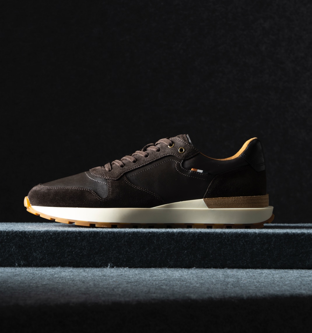 A side view of a men’s sneaker in dark brown suede. Vue latérale d'une basket pour homme en suède brun foncé.