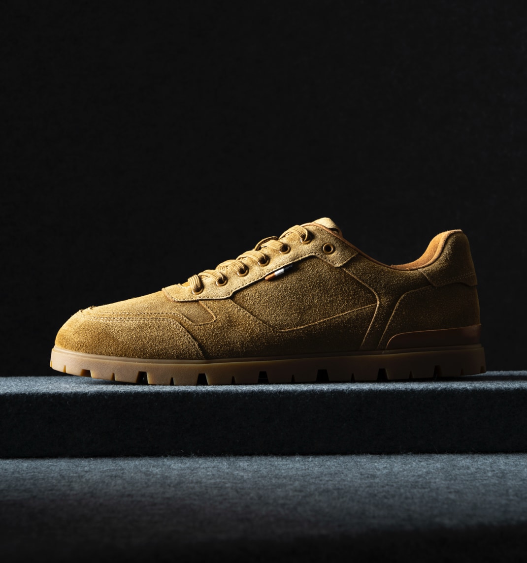 A side view of a men’s suede sneaker in tan with a lug sole. Vue latérale d'une sneaker en suède pour homme de couleur beige avec semelle crantée.